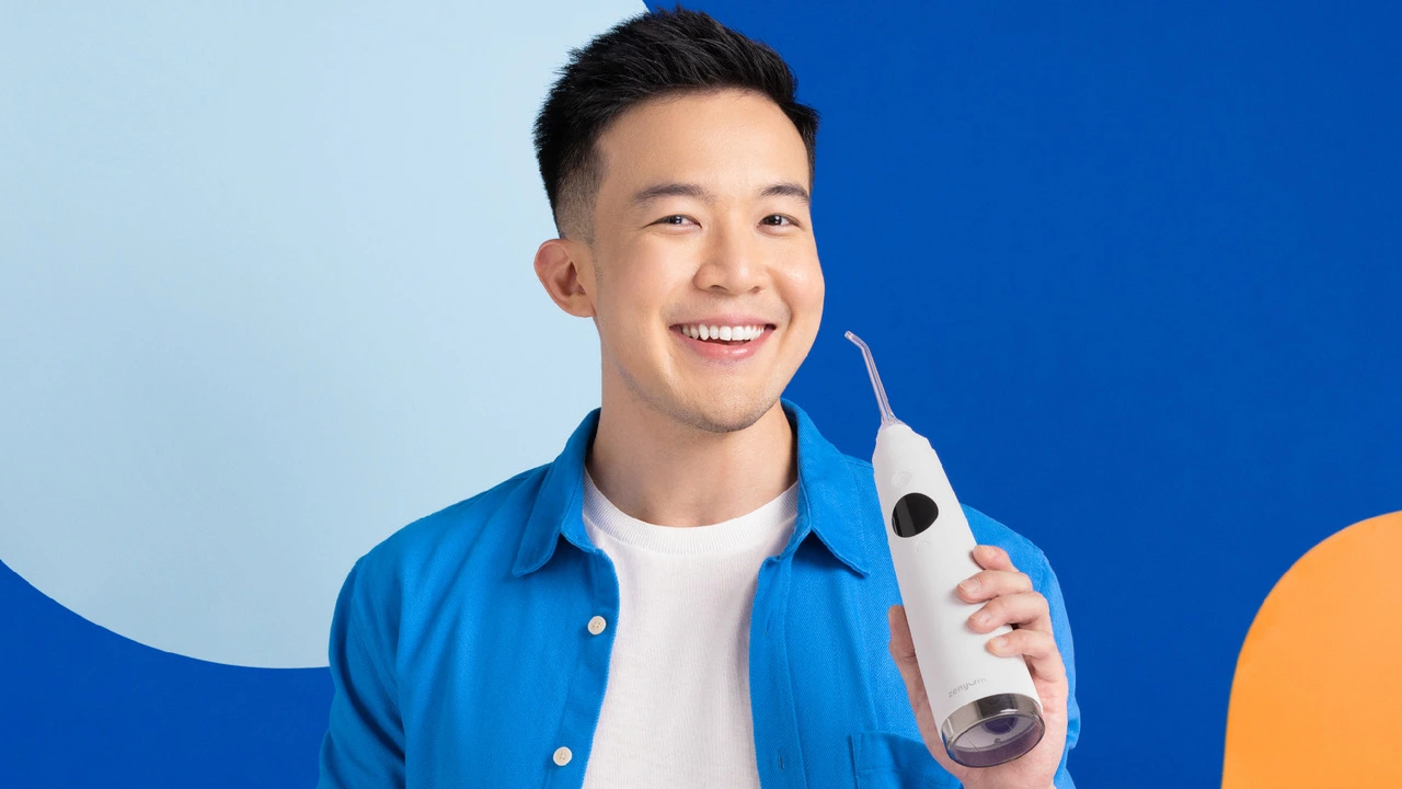 A man holding a water flosser and smiling against a blue background.