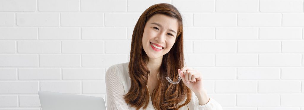 ผู้หญิงยิ้มถืออุปกรณ์จัดฟันใส Zenyum