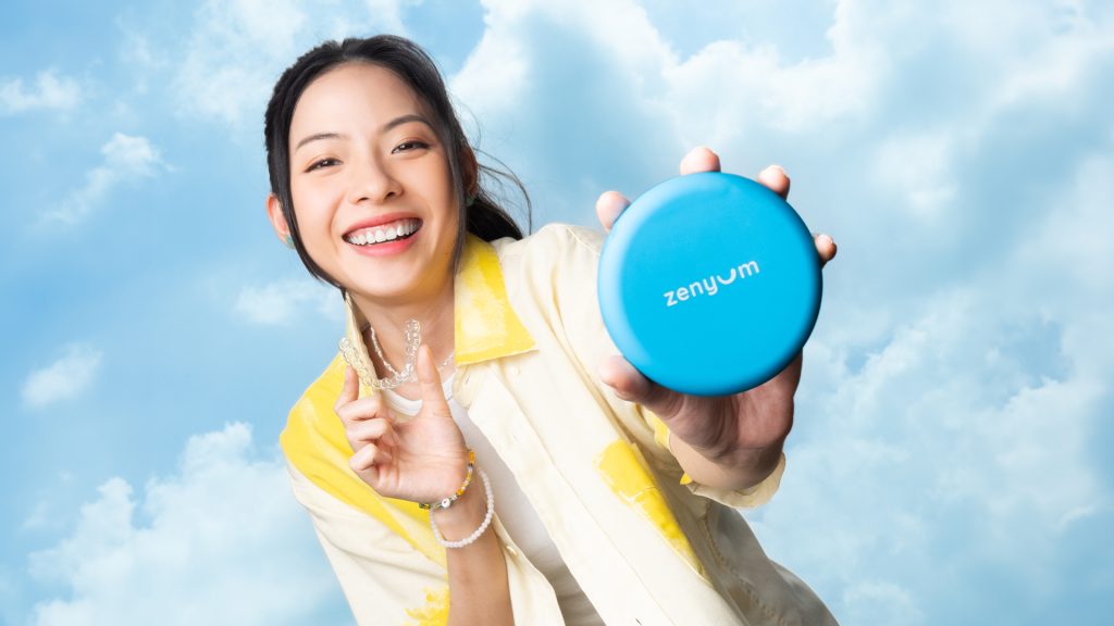 A woman joyfully holds a Zenyum clear aligner and aligner case.