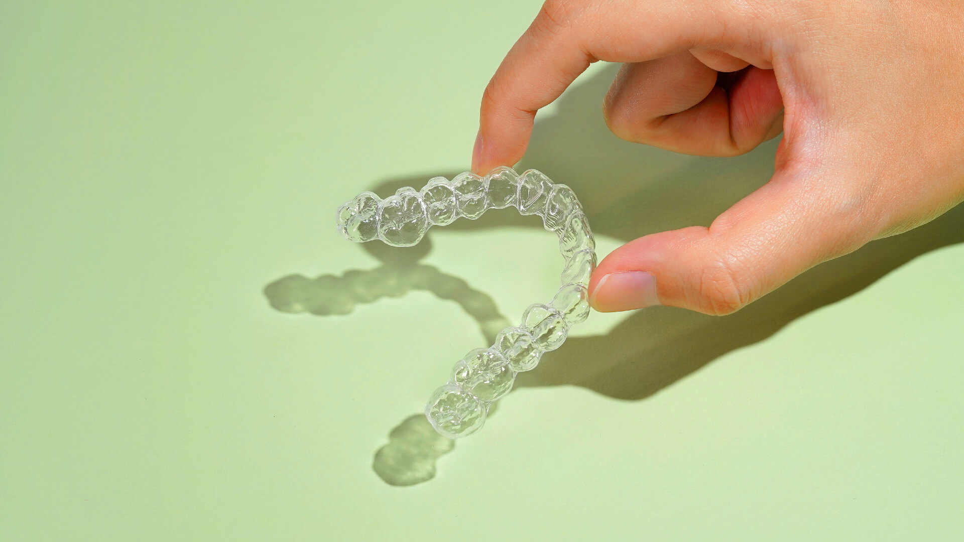 A hand holding Zenyum Clear Braces over a light green background