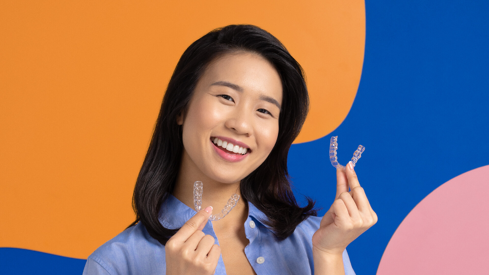 A smiling young person holding Zenyum aligners