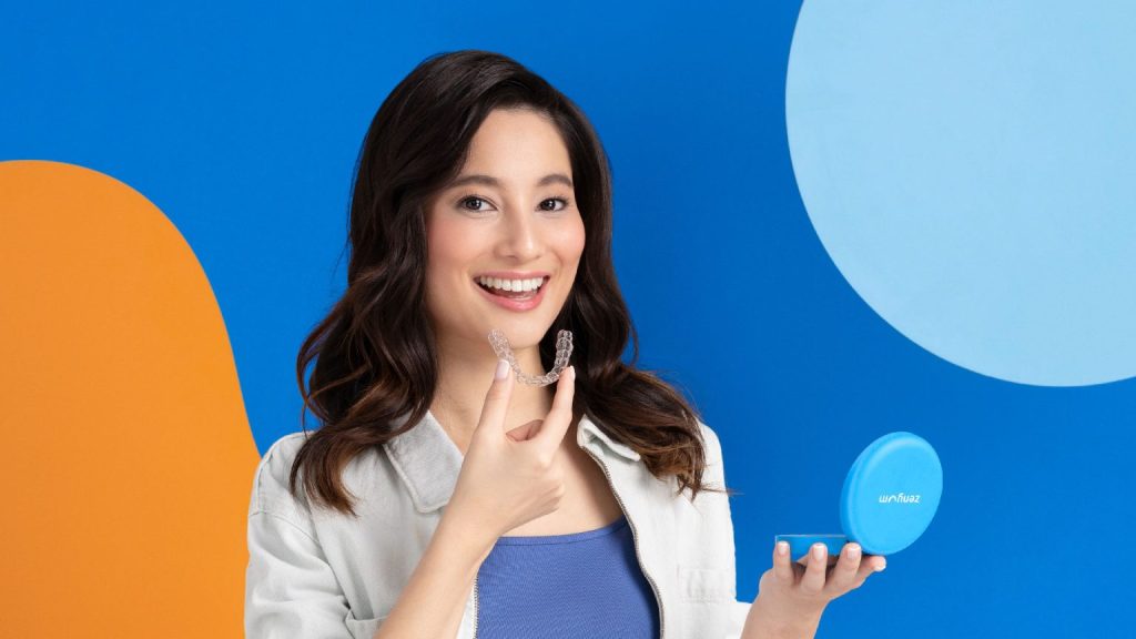 Female person smiling while holding clear aligners and holding blue aligner case