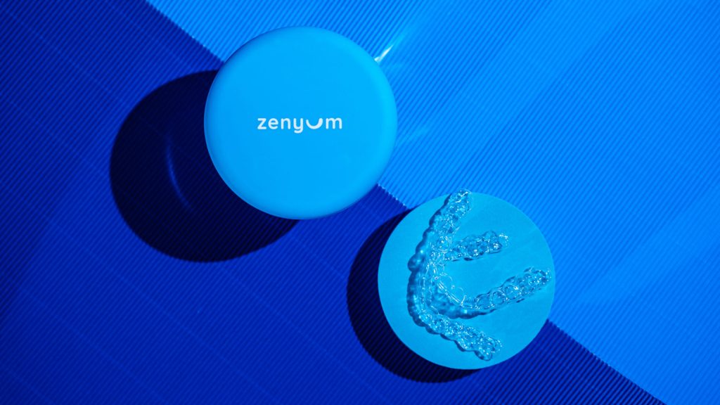 A pair of clear aligners that can treat overcrowded teeth and a blue Zenyum Invisible Braces case.
