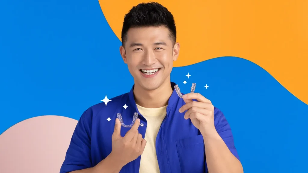A man holding up two Zenyum clear aligners against an orange and blue background.