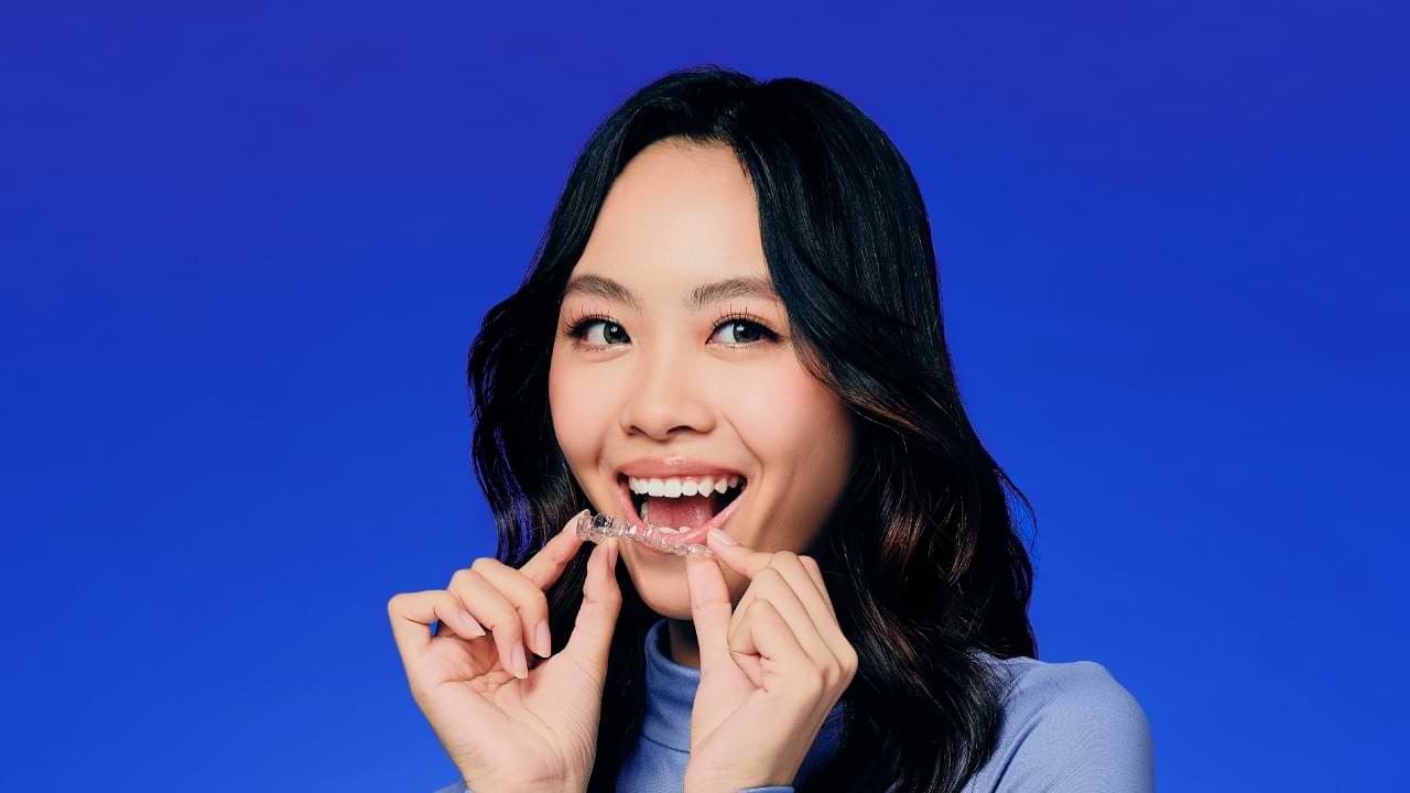 A smiley girl putting on clear aligner