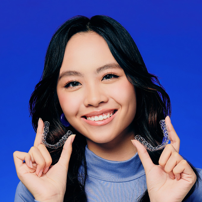 Girl in blue holding clear aligner