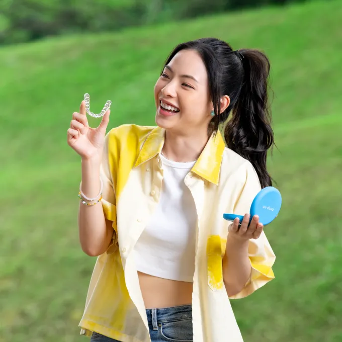 Girl in yellow holding clear aligner and Zenyum case